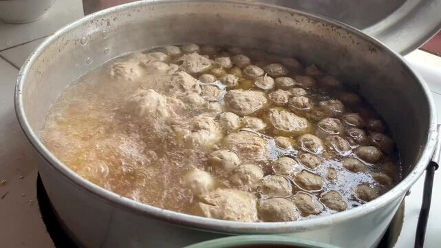 Boiling meatballs in an open hot pot and the boiling water erupts with hot steam. the process of boiling round meatballs