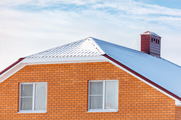 A brick house with a red roof and two windows