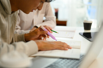 Close up shot of student highlighting important text with a marker while studying with his tutor