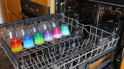 Open dishwasher with clean utensils in it with only colored glass cups.