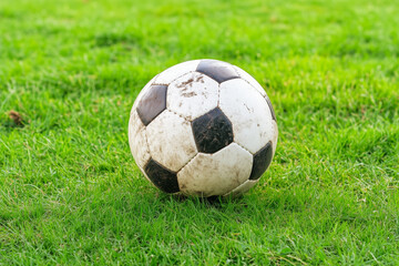 Fototapeta premium Worn black and white soccer ball resting on a vibrant green grass field