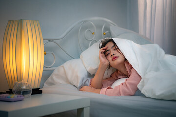 Asian young woman on the bed in the bedroom trying to wake up and prepare for work