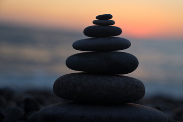 black silhouette of stack of pebble rocks on sunset beach background. Stones standing on top of each other against the backdrop of a sunrise on the seashore .