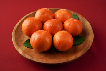 Ripe oranges served on wooden plate on red-clothed table. Isolated on red background. Chinese New Year Concept