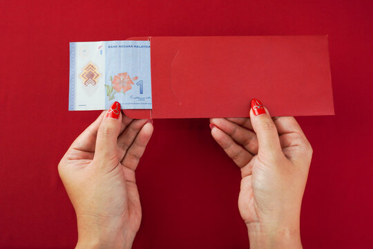 An unlucky Malaysian chinese woman opening a red envelope gift, only to find a very small amount of money inside, one ringgit. Concept for Chinese New Year.