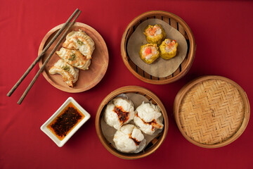 Asian women hand is picking dim sum using wooden chopsticks. Steamed dumplings for Chinese New Year party, isolated on red background.