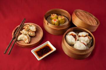 Asian women hand is picking dim sum using wooden chopsticks. Steamed dumplings for Chinese New Year party, isolated on red background.