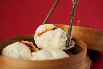 Asian women hand is picking dim sum using wooden chopsticks. Steamed dumplings for Chinese New Year party, isolated on red background.