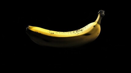 A solitary ripe banana with a smooth yellow peel is illuminated against a black background, highlighting its natural curves and spots.