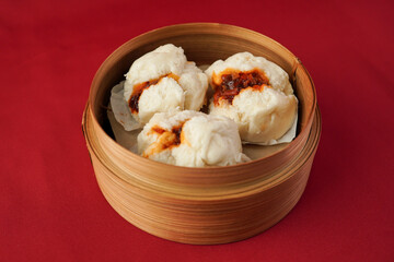 Steamed baozi dim sum on wooden plate isolated on red background. Steamed dumplings for Chinese New Year party.