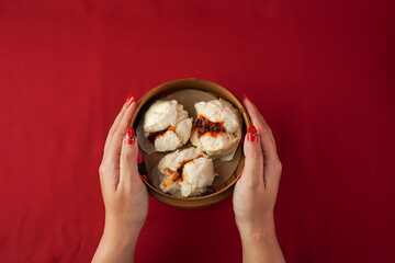 Asian women hand serving baozi dim sum using woven bamboo steamer plate. Steamed dumplings for Chinese New Year party, isolated on red background.