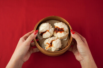 Asian women hand serving baozi dim sum using woven bamboo steamer plate. Steamed dumplings for...
