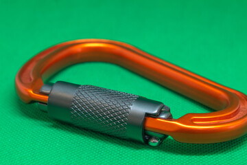 Metal orange carabiner for rock climbing on green background, isometric view
