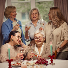 Cozy meeting with friends. Elderly women meeting in warmly-lit restaurant or home, drinking wine, talking and discussing news. Concept of elderly lifestyle, positive emotions