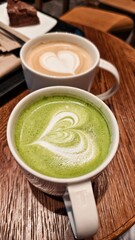Matcha tea and cappuccino coffee with heart shape drawing in ceramic mugs on the table
