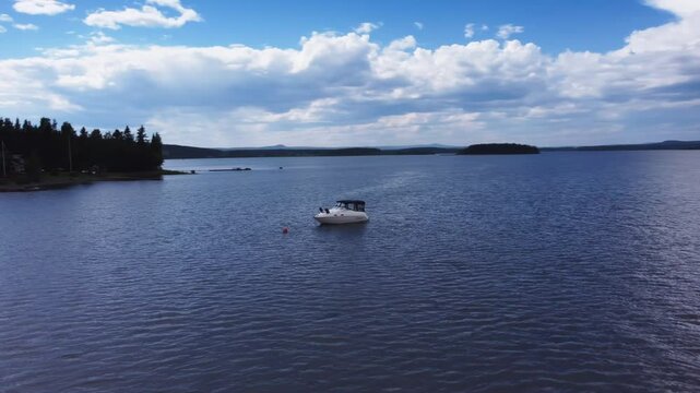 Aerial of an anchored boat in the water during a warm sunny summer day, with white clouds in the sky