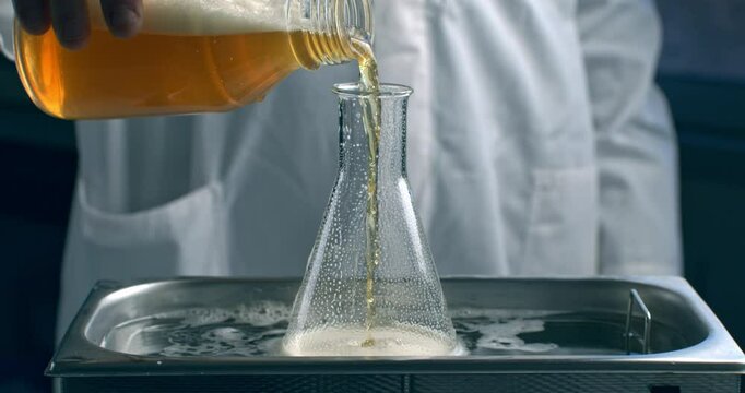 Super slow motion of lab worker pours beer into glassware for quality testing, ensuring it meets production standards. The beer is carefully inspected in brewery with precision and dedication.