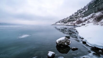 Obraz premium Winter landscape of Baikal Lake featuring icy shores and rocky outcrops under a cloudy sky near a remote island village