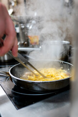 A hand using chopsticks to stir steaming pasta in a pan on a stovetop. The kitchen setting is filled with a warm, inviting atmosphere, emphasizing the art of cooking.