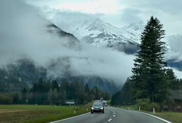 Vehicles drive up and down a two lane highway in the Italian Dolomites where mountains are dusted in snow.