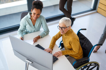 Disabled woman in wheelchair looking at computer, discussing startup project with interracial team