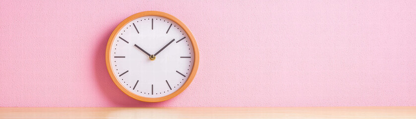 round wall clock with wooden frame shows time against pink background, creating cheerful and modern atmosphere