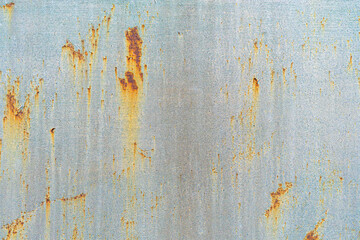 A close-up of a weathered metal surface with streaks of rust and faded paint. The textured details of corrosion and peeling color create an industrial, abstract background with an aged aesthetic