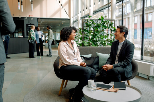 Happy male and female business professionals sitting on couch in lobby at convention center