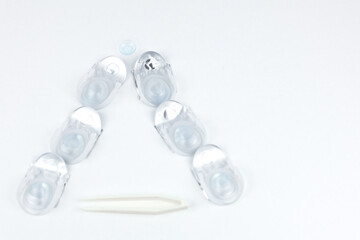 A Christmas tree made of containers with contact lenses lies on a white background, a lying lens is visible on top, and lens tweezers with space for text are at the bottom. High quality photo