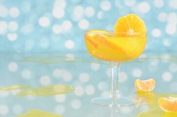 Orange cocktail with slices of tangerine and orange, empty space to fill with content, spilled orange juice, blurry lights in the background. 