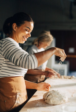 Smiling female baker during flour on kneaded dough while working at bakery