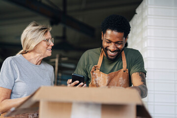 Smiling senior female baker talking with male colleague taking inventory while working at bakery