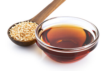 Sesame oil in a glass bowl and wooden spoon with sesame seeds isolated on white background. With clipping path.