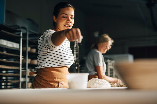 Female artisan dusting flour on dough while working at bakery