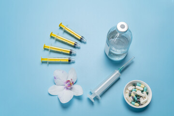 Bowl with capsules, a glass bottle with liquid medicine, big and small plastic syringes on the blue background.