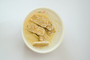Raw tempeh that has been cut in a white bowl containing dough, with a white background.