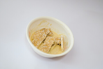 Raw tempeh that has been cut in a white bowl containing dough, with a white background.