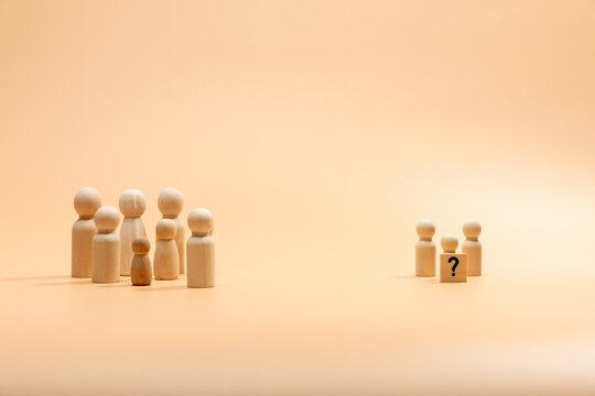 Two groups of wooden figures in the form of people. A large group and a small group with a question mark. The concept of finding oneself and finding communication with society.