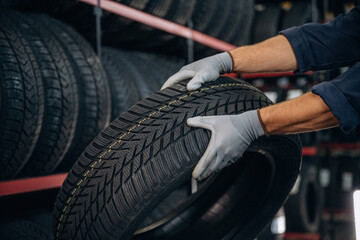 Fototapeta premium In grey gloves, taking the tire. Man worker is maintenance station with wheels