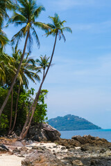 A rugged beach on Koh Samui, Thailand, showcasing dark volcanic rocks, patches of sand, and turquoise sea waters.