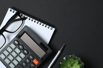 Top above overhead view photo of office accessories calculator, notebook and pen on black backdrop with blank empty space