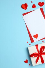 Gift box with red hearts, paper card and envelope on color background