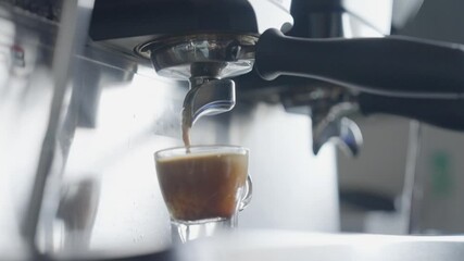 A handheld side angle mid-close-up slow-motion shot of coffee being poured into a coffee cup from a coffee machine at a cafe