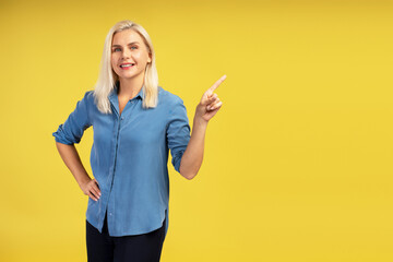 Smiling businesswoman pointing finger showing something on yellow background