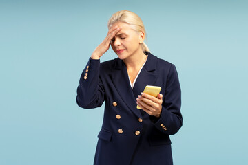 Stressed businesswoman having headache holding smartphone on blue background