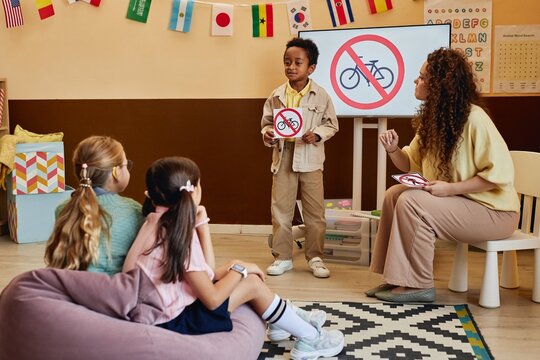 Full length portrait of young African American boy standing in front of class holding No bicycles sign while presenting road safety rules in school classroom
