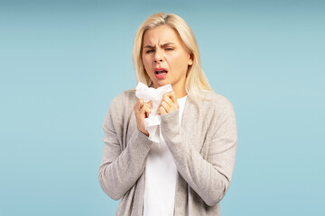 Sick woman blowing her nose with tissue on blue background