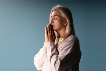 Senior woman praying with hope and faith on blue background