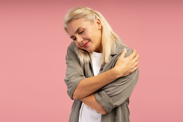 Blond woman hugging herself on pink background showing self love and acceptance