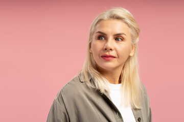 Blonde mature woman looking away on pink background in studio shot